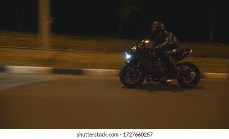 Man Riding Fast On Modern Black Sport Motorbike At Evening City Street. Motorcyclist Racing His Motorcycle On Night Empty Road. Guy Driving Bike With Headlight On. Concept Of Freedom. Side View.