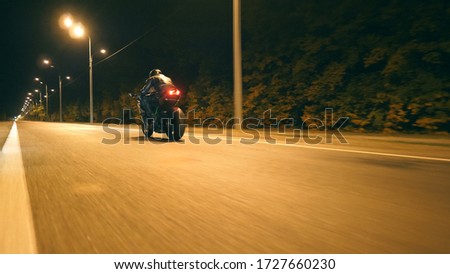 Man riding fast on modern sport motorbike at nighty city street. Motorcyclist racing his motorcycle on empty road. Guy driving bike at dusk. Concept of freedom and adventure. Low angle of view Closeup