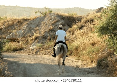 Man riding his horse in a path in the hills at sunset - Powered by Shutterstock