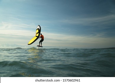 Man riding a hydrofoil surfboard using a hand held foil wing.