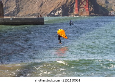 Man riding a hydrofoil surfboard using a hand held foil wing. 