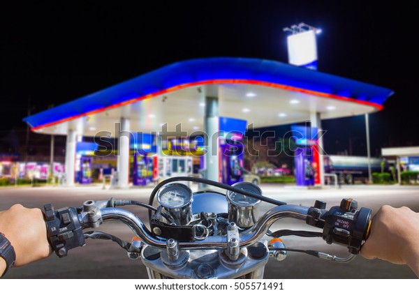 Man riding motorcycle, blur image of gas\
station as background.