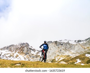 Man Riding A Mountain Bike In The Snowy Mountains, Wears A Mountain Bike And Winter Clothes, Helmet And Safety Protections