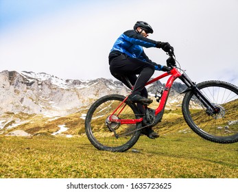 Man Riding A Mountain Bike In The Snowy Mountains, Wears A Mountain Bike And Winter Clothes, Helmet And Safety Protections