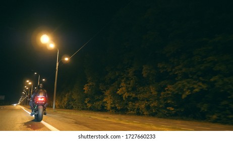 Man Riding On Modern Sport Motorbike At Night Street Of Town. Motorcyclist Racing His Motorcycle On Evening City. Guy Driving Bike During Trip. Concept Of Freedom And Adventure. Back View Close Up.