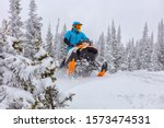 A man is riding snowmobile in mountains. jump on a snow bike.
pilot on a sports snowmobile in a mountain forest. The concept of skidooking. rider in a bright suit on a colorful snowy moto. Hi quality