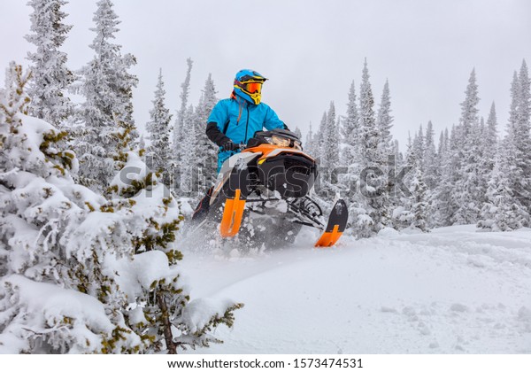 A man is riding snowmobile in mountains. jump on\
a snow bike.\
pilot on a sports snowmobile in a mountain forest.\
The concept of skidooking. rider in a bright suit on a colorful\
snowy moto. Hi quality
