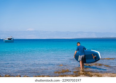 Man riding SUP stand up paddle on vacation. Active male riding SUP boards and paddling in the ocean on a sunny day. Athletic person on SUP board with yachts in background, Silba, Croatia. - Powered by Shutterstock