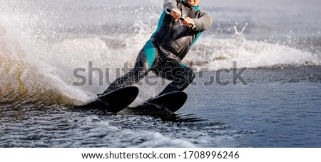 man riding water ski on summer lake. black neoprene wetsuit on full body