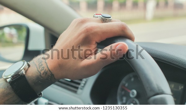A\
man with rings on his hand drives a car. Hand\
close-up.