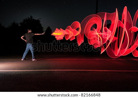 A man in the road at the middle of the night shooting out a graffiti-like artistic laser blast powers from his hand