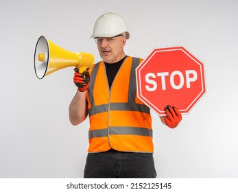 Man in road worker's uniform. Builder with loudspeaker. Road worker shows stop sign. Portrait of road repairman with loudspeaker. Builder shouts into megaphone. Man builder on light background - Powered by Shutterstock