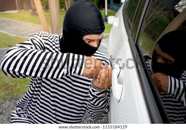 The man robber with a balaclava on his head\
trying to break into the car. He uses a screwdriver/Selective\
focus/Criminal and car thief\
concept