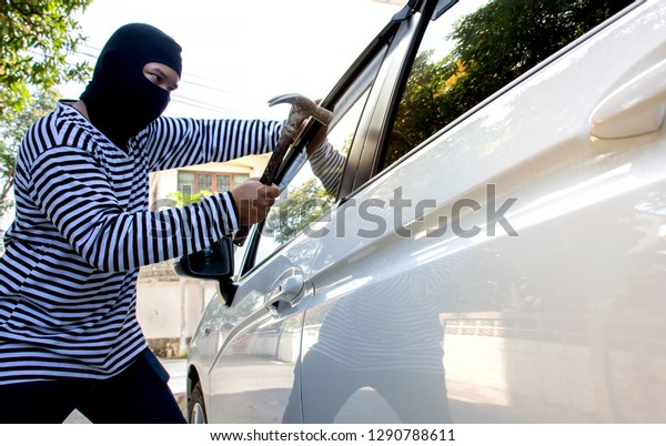 The man robber with a balaclava on his head\
holding a hammer trying to break into the car/Selective\
focus/Criminal and car thief\
concept