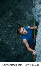 man rock climber with long hair. young man rock climber in bright red shorts and blue t-shirt climbing the challenging route on the cliff. rock climber climbing on a limestone wall. man making hard