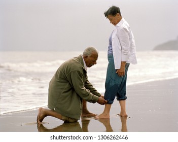 Man rolling up his wife's jeans at the beach. - Powered by Shutterstock