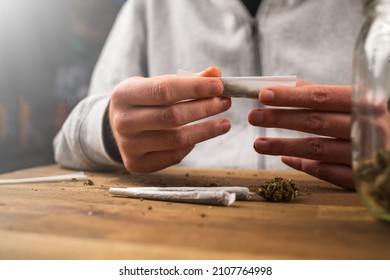 Man Rolling Marijuana Cannabis Joint In Coffee Shop Amsterdam With CBD Weed Buds In Glass Jars.