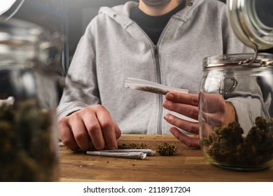 Man Rolling Marijuana Cannabis Joint In Coffee Shop Amsterdam With CBD Weed Buds In Glass Jars.