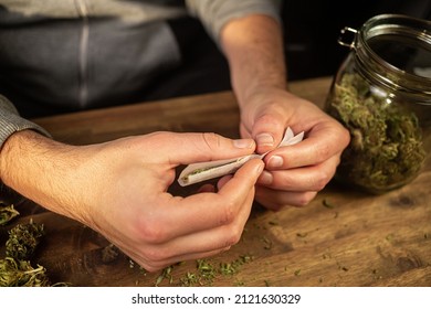 Man Rolling Marijuana Cannabis Joint In Coffee Shop Amsterdam With CBD Weed Buds In Glass Jars.