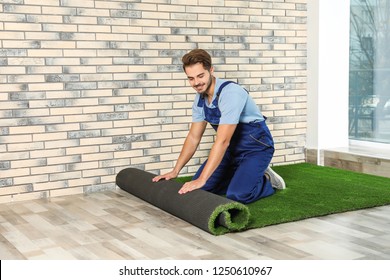 Man rolling out artificial grass carpet indoors. Space for text