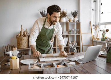 Man rolls clay with rolling pin in a bright and cozy pottery studio. He is concentrated on his work, surrounded by various pottery tools and equipment, creating a relaxed and creative atmosphere. - Powered by Shutterstock