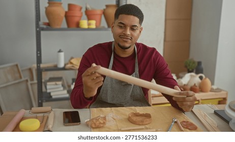 Man rolls clay with a rollingpin while holding it between both hands in studio; focused craftsmanship.
