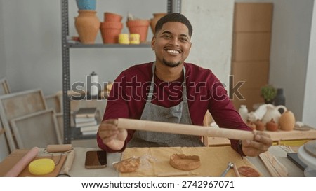 Man rolls clay with a rollingpin while holding it between both hands in studio; focused craftsmanship.