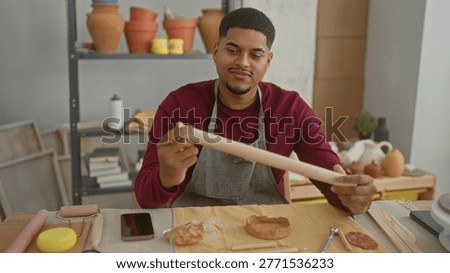 Man rolls clay with a rollingpin while holding it between both hands in studio; focused craftsmanship.