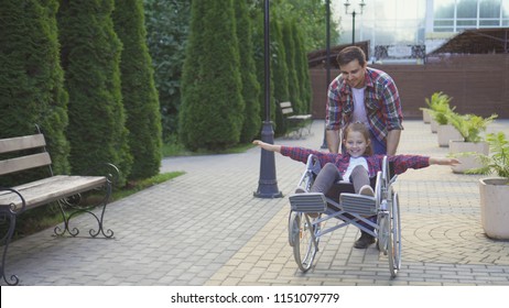 Man rolls a happy teenager in a wheelchair in the Park