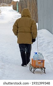 A Man Rolls A Sled With Empty Plastic Bottles Along A Snow-covered Alley