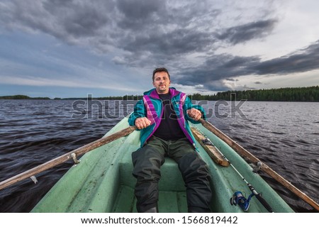 Man row a small wooden rowboat dinghy over calm water in the lake.