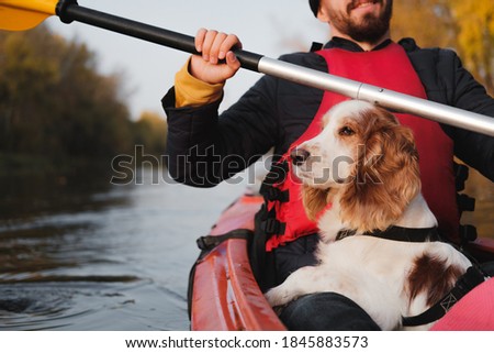 Man rowing a canoe with his spaniel dog, sunny autumn weather. Going kayak boating with dogs on the river, active pets, happy dog and owner on an adventure