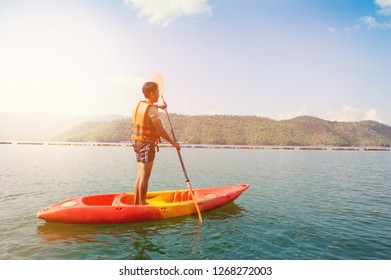 Man Rowing With A Paddle On The Stand Up On Kayak With Mountain Landscape View