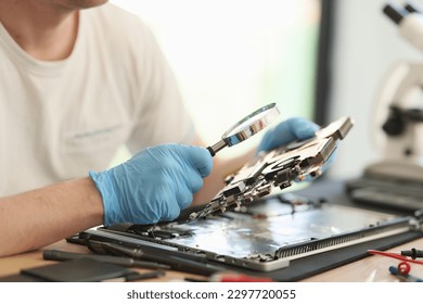 Man in rubber gloves looks at printed circuit board of laptop through magnifier glass. Electronic devices repair service and maintenance - Powered by Shutterstock