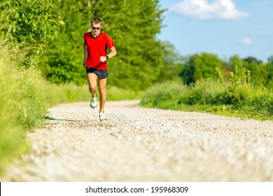 Man runner running on country road in summer sunset. Young athlete male cross country training and doing workout outdoors in green nature, summer blue sky
