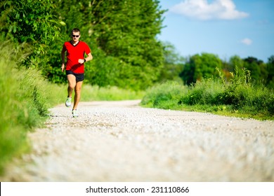 Man runner running on country road in summer sunset. Young athlete male training and doing workout outdoors in nature.
