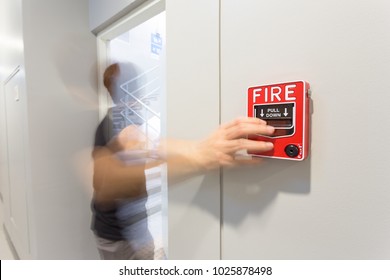 The Man Running And Hand Is Pulling Fire Alarm On The Wall Next To The Emergency Exit Door.