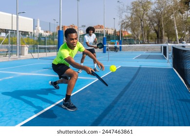 Man running to reach a ball playing pickleball with friend in an outdoor court - Powered by Shutterstock