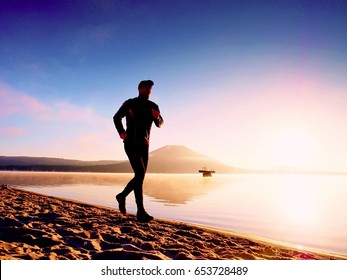 Man running at seaside twilight time. Runner athlete running at seaside. Sportsman fitness silhouette sunrise jogging workout wellness concept. 