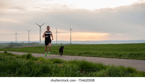 a man runs along the green field with a dog, with a view of the windmills