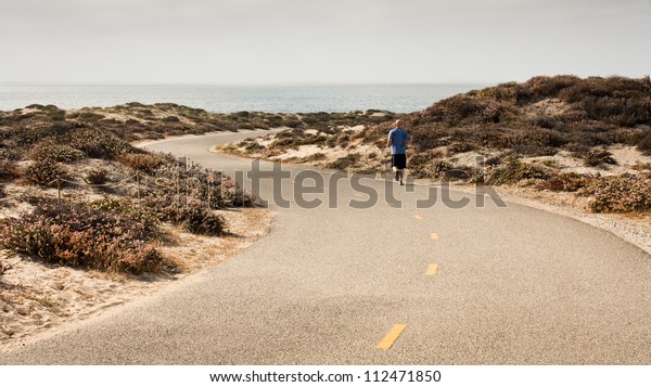 A man runs\
along a paved recreation trail in a sand dune area adjacent to\
Monterey Bay in Monterey\
County