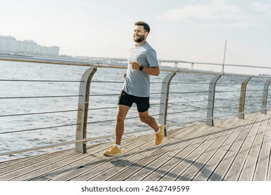 A man runs along a wooden boardwalk by the water, with a bridge and city skyline visible in the background. He is dressed in athletic attire, looking focused and enjoying the sunny weather.

 - Powered by Shutterstock