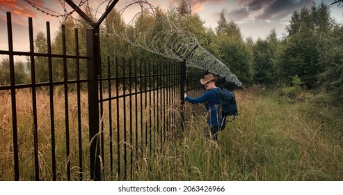 Man Runs To The Fence With Barbed Wire And Climbs On It. Evening Sunset. The Concept Of Illegal Border Crossing, Penetration Into A Protected Object And Unlawful Migration