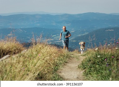 Man runs with his dog on the green meadow in mountain