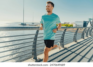 A man runs on a sunny waterfront path, wearing a turquoise shirt and black shorts, enjoying the scenic view.

 - Powered by Shutterstock