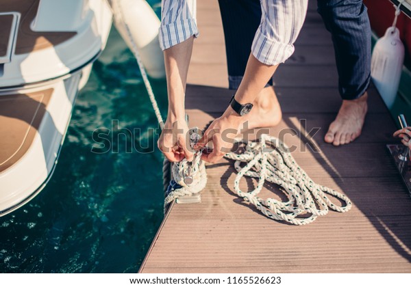Man s hand with boat\
rope. Yachtsman moors his motor boat at jetty. Close up hands and\
bow of the boat.