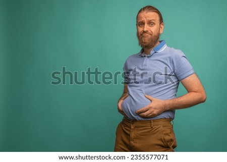 A man with a sad face feels his fat belly on blue background, closeup. Space for text