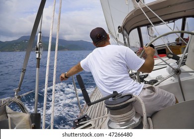 Man sailing a sailboat in the tropics with tropical mountain in background.