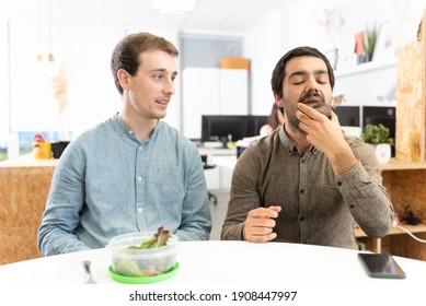 A Man With A Salad Looking With Envy To His Coworker Eating A Sweet Food In The Office.