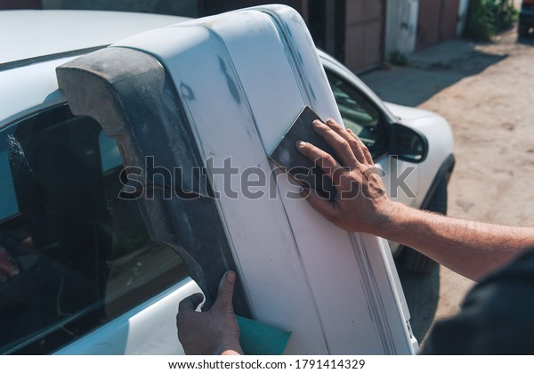 Man sanding the bumper from the car. Car\
maintenance and repair in the\
garage